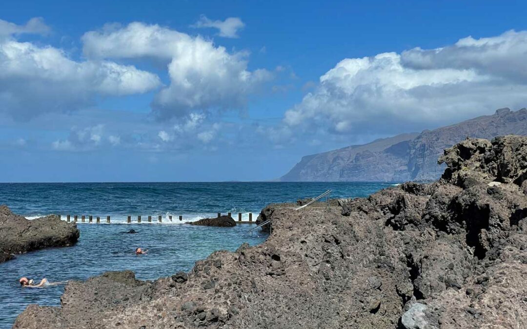 Menschen schwimmen in einem Naturpool auf Teneriffa, im Hintergrund sind das Meer und Steilklippen zu sehen.