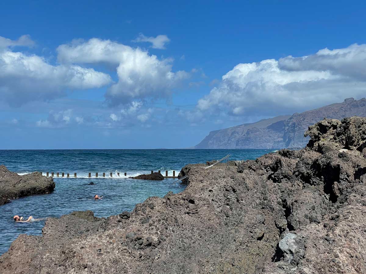 Menschen schwimmen in einem Naturpool auf Teneriffa, im Hintergrund sind das Meer und Steilklippen zu sehen.